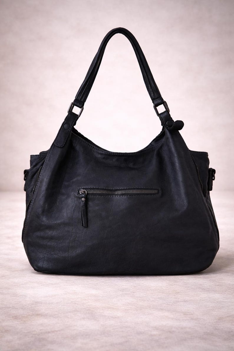 May include: Black leather shoulder bag with a zippered front pocket and two top handles. The bag has a slouchy design and a zipper closure. The bag is made of a soft, textured leather.