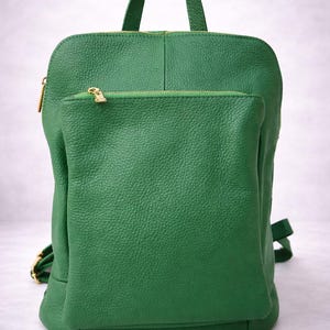 K&ouml;nnte beinhalten: Ein gr&uuml;ner Lederrucksack mit einer Rei&szlig;verschlusstasche vorne und einem oberen Griff. Der Rucksack hat goldfarbene Rei&szlig;verschl&uuml;sse und Beschl&auml;ge. Die Tasche hat verstellbare Schultergurte.