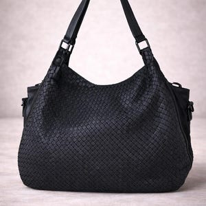 May include: A black woven leather handbag with a shoulder strap. The bag has a large, rounded shape with a woven pattern and a top handle. The bag is sitting on a neutral surface.