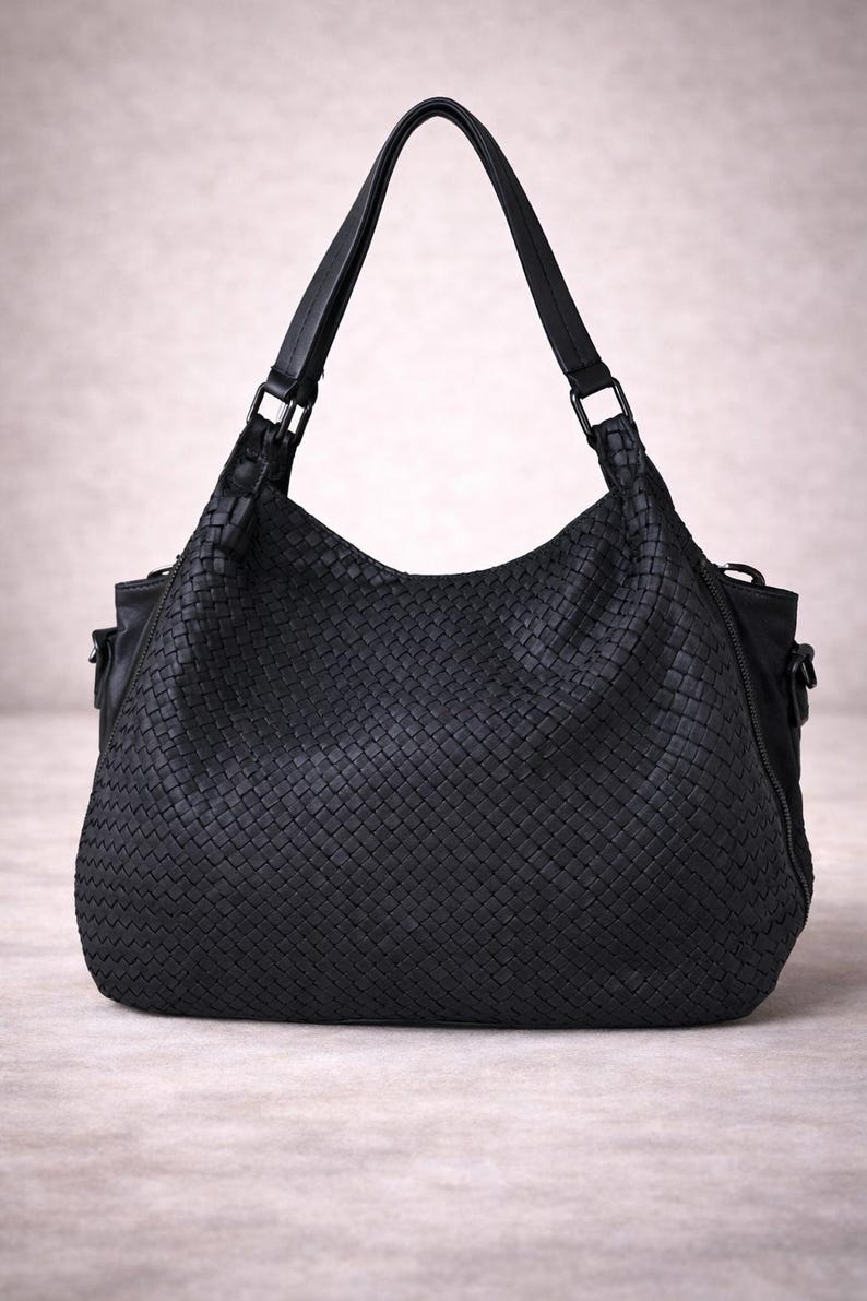 May include: A black woven leather handbag with a shoulder strap. The bag has a large, rounded shape with a woven pattern and a top handle. The bag is sitting on a neutral surface.