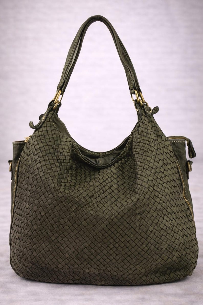 May include: Olive green woven leather handbag with two handles and gold-tone hardware. The bag has a large, rounded shape with a zipper closure and a woven texture throughout. The bag is designed for carrying items.