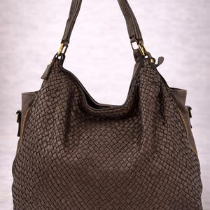 May include: A brown woven leather handbag with a shoulder strap and gold-toned hardware. The bag has a large, open top and a zippered side pocket. The woven texture gives the bag a unique, stylish look.