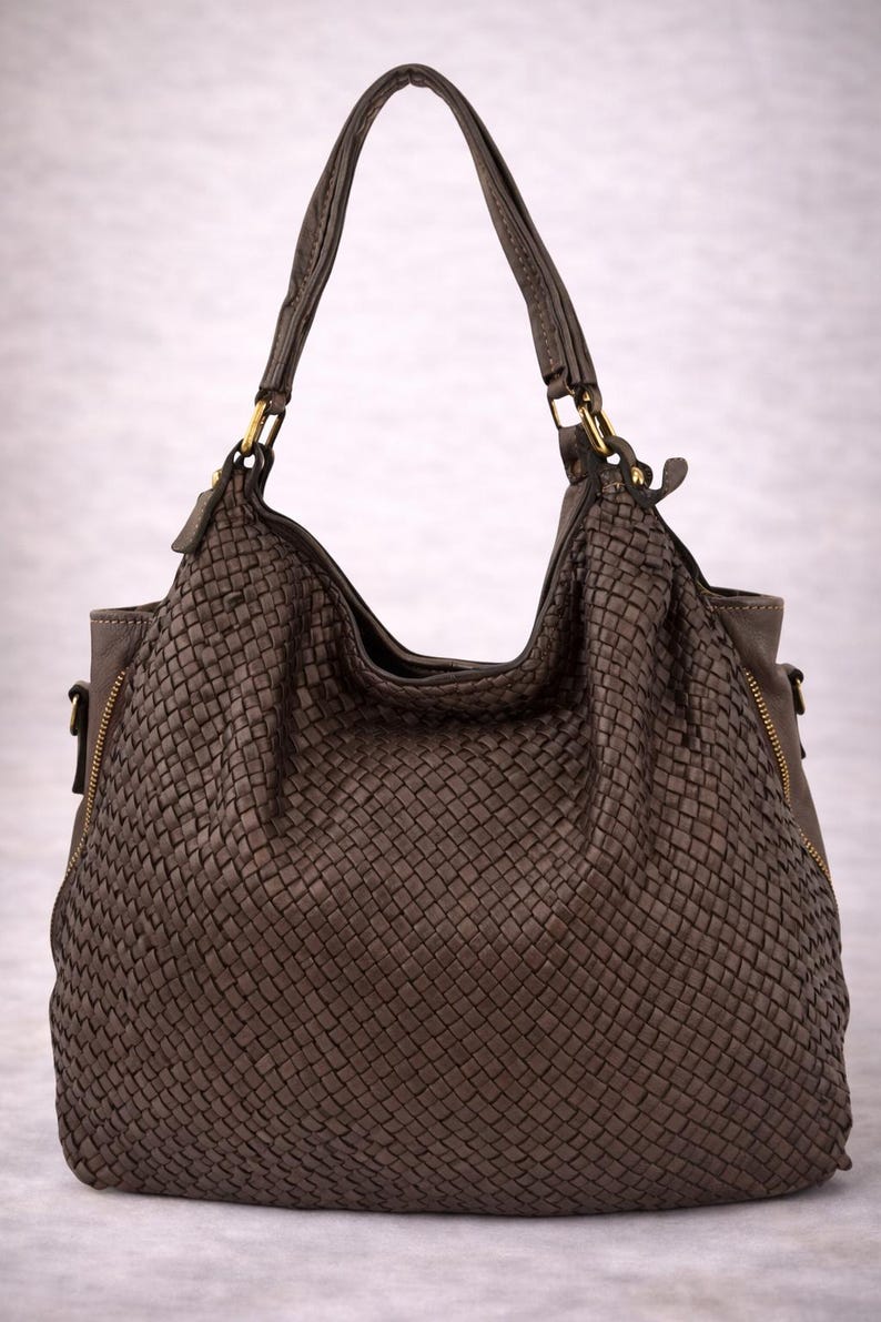May include: A brown woven leather handbag with a shoulder strap and gold-toned hardware. The bag has a large, open top and a zippered side pocket. The woven texture gives the bag a unique, stylish look.