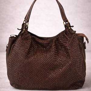 May include: A brown leather handbag with a woven design. The bag has a rounded shape, a top handle, and a shoulder strap. It features a zipper closure and gold-colored hardware.