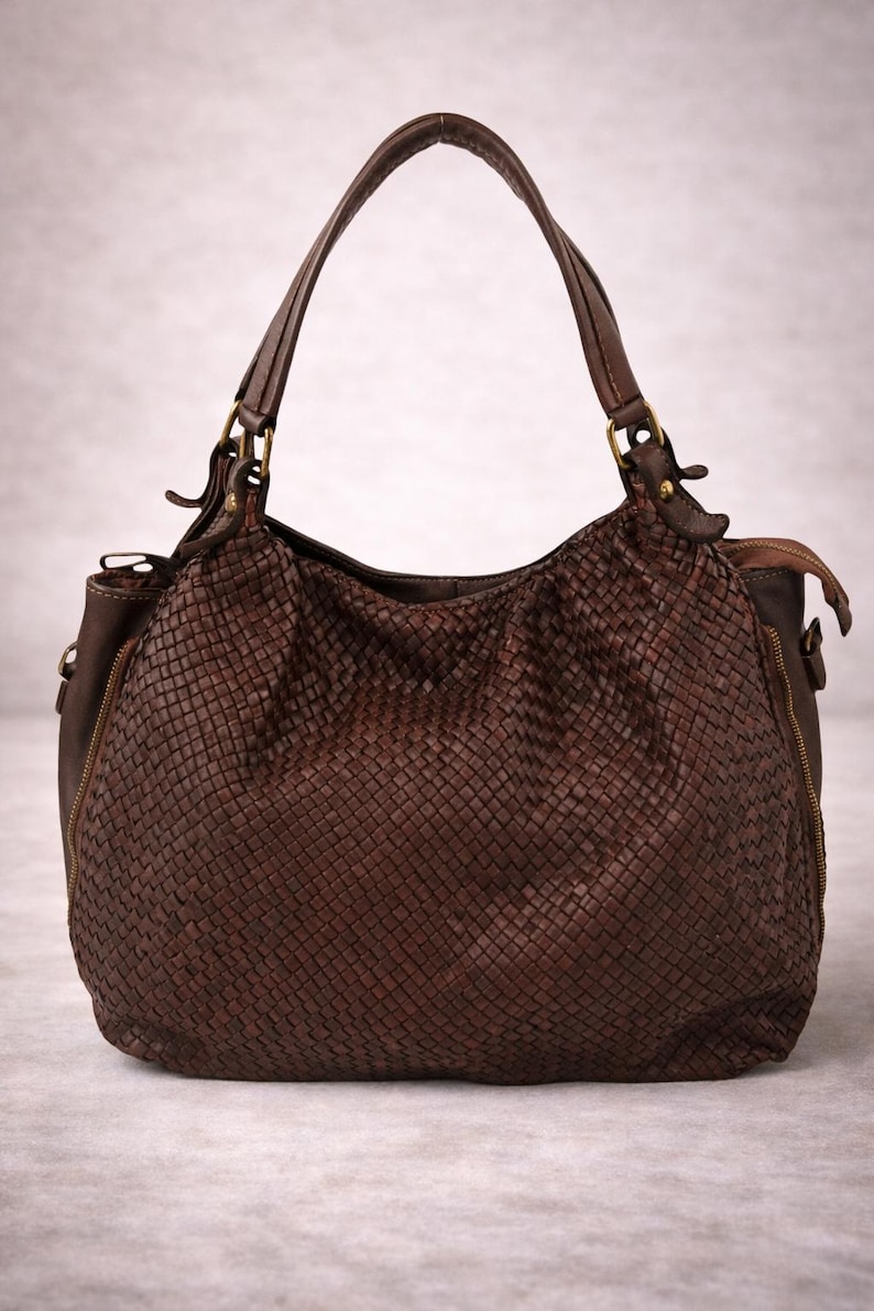 May include: A brown leather handbag with a woven design. The bag has a rounded shape, a top handle, and a shoulder strap. It features a zipper closure and gold-colored hardware.