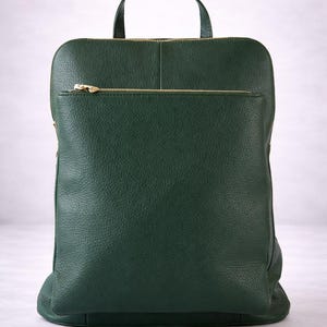 K&ouml;nnte beinhalten: Ein dunkelgr&uuml;ner Lederrucksack mit einem oberen Griff und einer Rei&szlig;verschlusstasche vorne. Der Rucksack hat einen goldfarbenen Rei&szlig;verschluss und eine strukturierte Oberfl&auml;che. Die Tasche hat eine rechteckige Form.