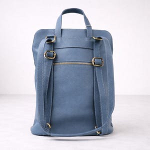 K&ouml;nnte beinhalten: Ein blauer Lederrucksack mit verstellbaren Schultergurten und einem oberen Griff. Die Tasche verf&uuml;gt &uuml;ber goldfarbene Hardware, einschlie&szlig;lich Schnallen und einem Rei&szlig;verschluss. Das Design ist schlicht und funktional, geeignet f&uuml;r den t&auml;glichen Gebrauch.