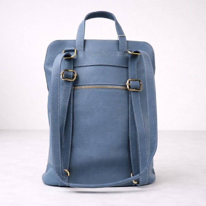 K&ouml;nnte beinhalten: Ein blauer Lederrucksack mit verstellbaren Schultergurten und einem oberen Griff. Die Tasche verf&uuml;gt &uuml;ber goldfarbene Hardware, einschlie&szlig;lich Schnallen und einem Rei&szlig;verschluss. Das Design ist schlicht und funktional, geeignet f&uuml;r den t&auml;glichen Gebrauch.