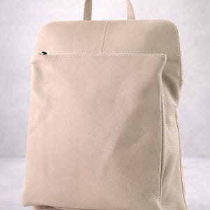 K&ouml;nnte beinhalten: Beigefarbener Lederrucksack mit oberem Griff und Vordertasche. Die Tasche hat eine rechteckige Form mit abgerundeten Ecken und einen Rei&szlig;verschluss an der Vordertasche. Das Leder hat ein strukturiertes Aussehen.
