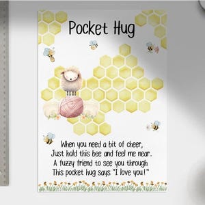 Può includere: Una stampa stravagante intitolata "Pocket Hug" presenta una pecora sopra un gomitolo di lana, circondata da api e un motivo a nido d'ape. Il testo recita: "Quando hai bisogno di un po' di allegria..." e "Ti amo!"