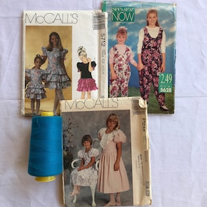 May include: Four sewing patterns for children's clothing. The patterns are from McCall's and See & Sew Now. The patterns feature a variety of styles, including dresses, overalls, and a jumper. The patterns are in various colors, including pink, blue, and green.