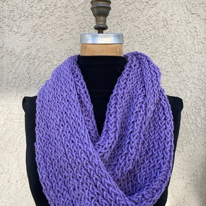 May include: A purple knitted infinity scarf. The scarf is made of a soft, chunky yarn and has a simple, elegant design.
