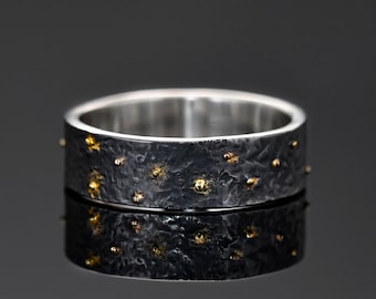 May include: A black and silver ring with a textured surface and gold accents. The ring is wide and has a flat band.