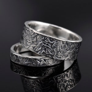May include: Two silver wedding bands with a textured, geometric pattern. The bands are stacked on top of each other.