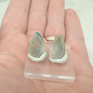 Op de afbeelding: Twee kleine, geode-achtige objecten in lichtgroen en wit staan op een heldere, rechthoekige basis. De geodes zijn gemonteerd op een witte, afgeronde basis. De afbeelding is genomen vanuit een close-up perspectief.