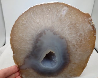 May include: A large, natural agate geode with a light brown exterior and a hollow center lined with white and gray crystals. The geode is sliced in half, revealing the intricate patterns of the crystals.