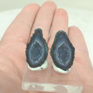 Op de afbeelding: Twee geode schijfjes met een donkerblauwe binnenkant en een sprankelend kristallen centrum. De randen zijn donkergroen en rood, geplaatst op een heldere rechthoekige basis. De geodes worden tegen een lichte achtergrond getoond.