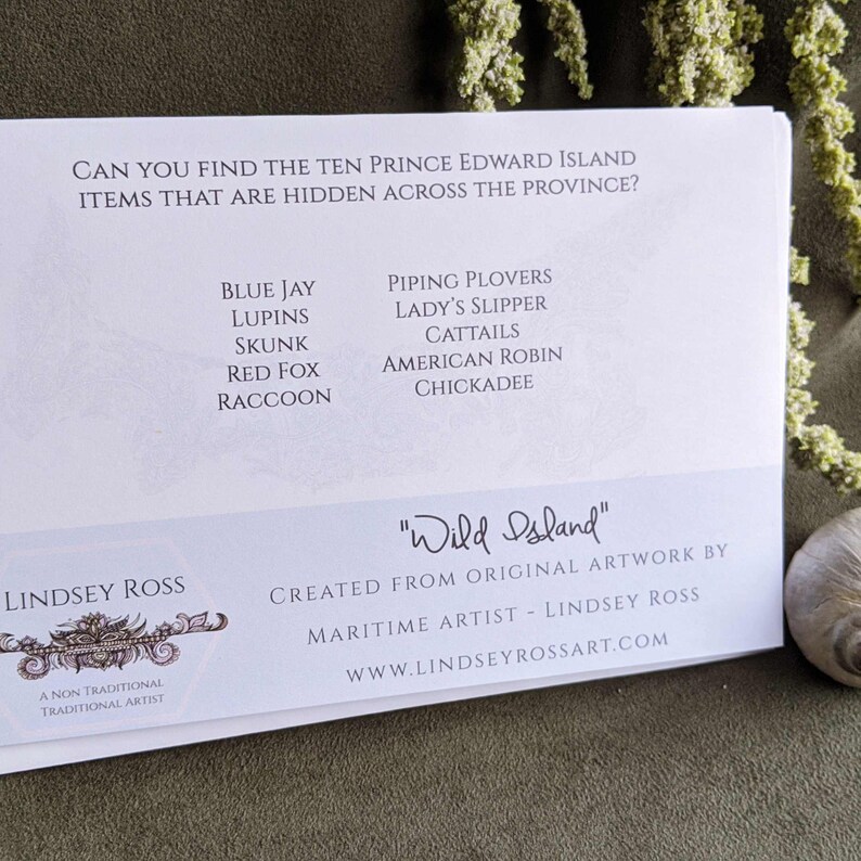 May include: A white card with blue text lists ten Prince Edward Island items, including blue jay, lupins, skunk, red fox, raccoon, piping plovers, lady's slipper, cattails, American robin, and chickadee. The card also features the text "Wild Island" and "Lindsey Ross, a non-traditional traditional artist".