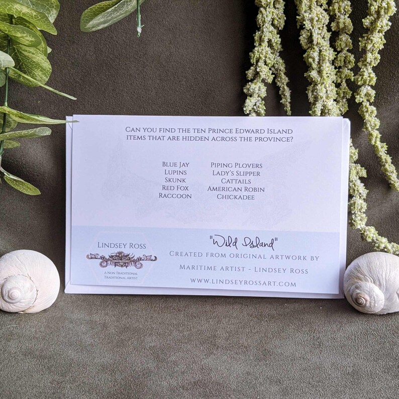 May include: White card with blue text that reads "Can you find the ten Prince Edward Island items that are hidden across the province?"  The card lists ten items: Blue Jay, Lupins, Skunk, Red Fox, Raccoon, Piping Plovers, Lady's Slipper, Cattails, American Robin, Chickadee.  The card also has the text "Lindsey Ross" and "Wild Island" with a website address.