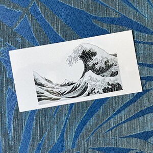 K&ouml;nnte beinhalten: Ein Schwarzwei&szlig;druck einer gro&szlig;en Welle, die gegen eine Bergkette kracht. Die Welle ist im traditionellen japanischen Stil dargestellt, mit wirbelnden Linien und schaumigen K&auml;mmen.