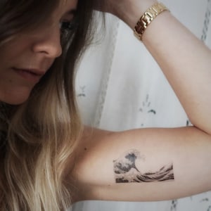 K&ouml;nnte beinhalten: Ein schwarz-wei&szlig;es tempor&auml;res Tattoo einer gro&szlig;en Welle, die bricht. Das Tattoo befindet sich auf dem Arm einer Person.