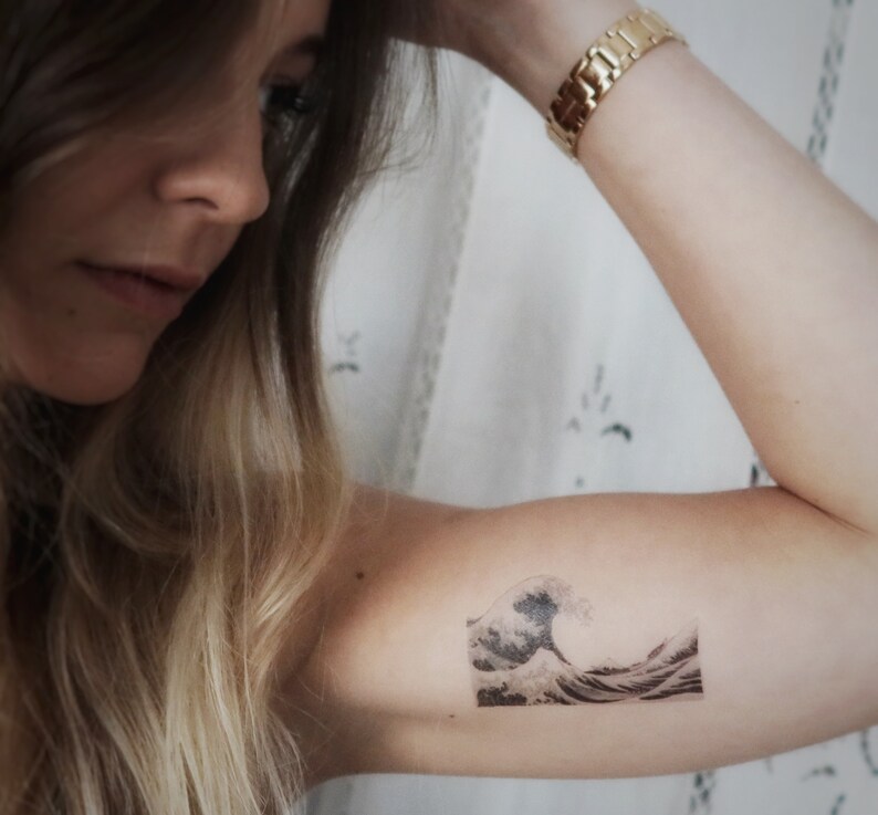 K&ouml;nnte beinhalten: Ein schwarz-wei&szlig;es tempor&auml;res Tattoo einer gro&szlig;en Welle, die bricht. Das Tattoo befindet sich auf dem Arm einer Person.