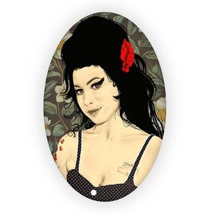 May include: Oval-shaped artwork featuring a portrait of a woman with black hair, a red flower, and a black polka dot top. The background has a floral pattern. The word "Blak" is visible on the chest.