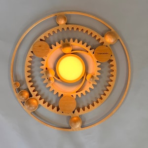 May include: A wooden wall art piece with a circular design featuring multiple gears and a central light. The piece is made of light wood and has a warm, natural aesthetic. The text "SYSTEM.ZONKEY" is visible on the piece.