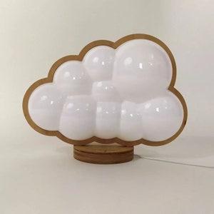 May include: A white cloud-shaped night light with a wooden base. The light is made up of several rounded shapes that resemble clouds.