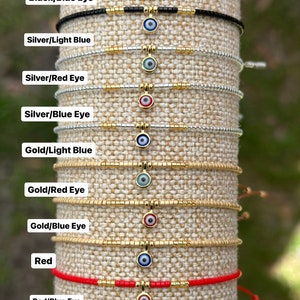 May include: A set of ten beaded bracelets with a gold evil eye charm. The bracelets are in various colors, including black, silver, gold, and red. The evil eye charms are blue, red, and light blue.