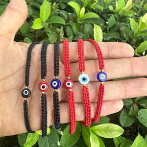 May include: Five red and black string bracelets with an evil eye charm. The charms are blue, black, and red with a gold rim.