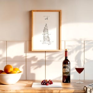 May include: A framed print with a black and white illustration of a stack of dishes and the text "Let's call it art". A bottle of red wine and a glass of red wine are on a wooden table with a white cutting board and a bowl of oranges.