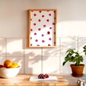 Puede incluir: Una impresi&oacute;n enmarcada con fondo blanco y un patr&oacute;n repetido de frambuesas rosas. La impresi&oacute;n est&aacute; colgada en una pared de azulejos blancos.