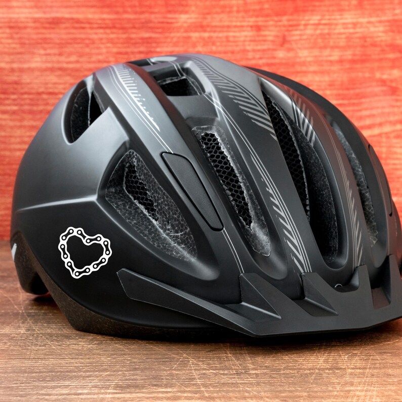 Puede incluir: Casco de bicicleta negro con una pegatina en forma de coraz&oacute;n de eslabones de cadena. El casco tiene orificios de ventilaci&oacute;n y rayas plateadas. Dise&ntilde;ado para la seguridad y protecci&oacute;n durante el ciclismo.