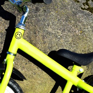 Puede incluir: Una bicicleta de equilibrio verde ne&oacute;n con un asiento y neum&aacute;ticos negros. La bicicleta tiene un manillar plateado y una pegatina de carita sonriente negra en el cuadro. Dise&ntilde;ada para ni&ntilde;os peque&ntilde;os.