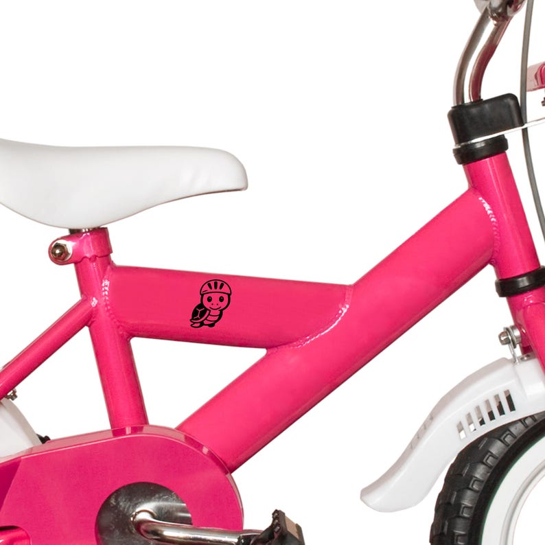 Puede incluir: Una bicicleta rosa brillante para ni&ntilde;os con un sill&iacute;n y guardabarros blancos. Una tortuga de dibujos animados negra con casco est&aacute; en el cuadro. El manillar es plateado y los neum&aacute;ticos son negros con laterales blancos.