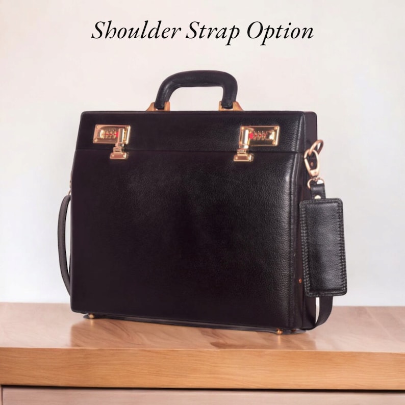 May include: Black leather briefcase with gold-colored hardware, including two combination locks. Features a top handle and a detachable shoulder strap. The text "Shoulder Strap Option" is visible above the briefcase.