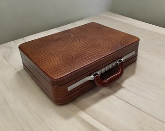 May include: A brown leather briefcase with a silver metal handle and clasps. The briefcase has a crocodile-embossed pattern.