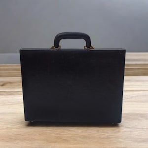 May include: A black briefcase with a handle and gold-colored accents. The briefcase is rectangular and appears to be made of leather or a similar material. The handle is padded for comfort.