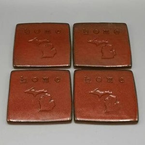 May include: Set of four terracotta coasters with a raised outline of the state of Michigan and the word "home" in a brown glaze.