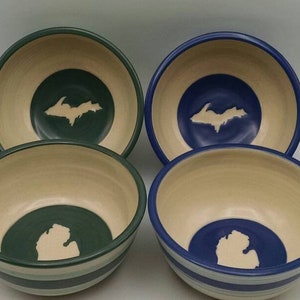 May include: Four ceramic bowls with a white outline of the Upper Peninsula of Michigan on a green and blue background. The bowls have a white rim and a white stripe around the bottom.