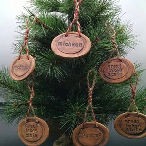 May include: A Christmas tree decorated with handmade clay ornaments. The ornaments are brown and feature the words "Michigan" and "Great Lakes State".