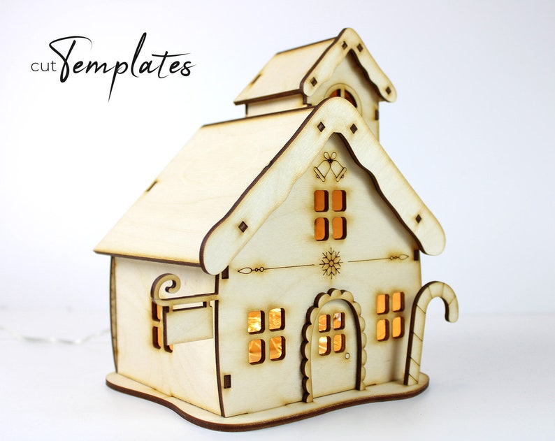 Puede incluir: Una casa de Navidad de madera con un dise&ntilde;o de bast&oacute;n de caramelo, copo de nieve y campana. La casa tiene ventanas con luces en el interior.