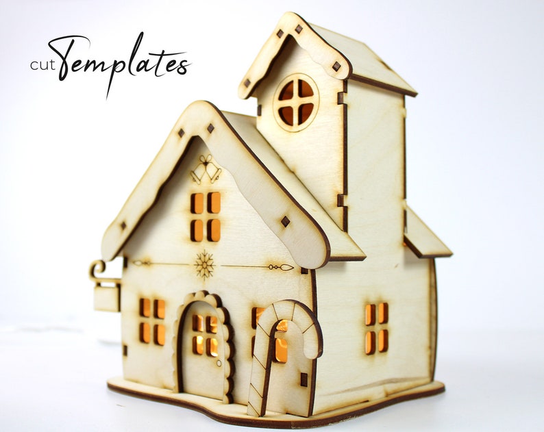 Puede incluir: Una casa de Navidad de madera con una torre, ventanas y una puerta. La casa est&aacute; iluminada desde el interior, creando un brillo c&aacute;lido. La casa est&aacute; hecha de madera marr&oacute;n claro y tiene un techo blanco.