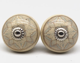 May include: Two ceramic knobs with a white background and a light blue and gold intricate design. The knobs have a silver metal centre.