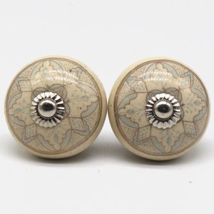 Peut inclure: Deux boutons en céramique avec un fond blanc et un motif complexe bleu clair et or. Les boutons ont un centre en métal argenté.