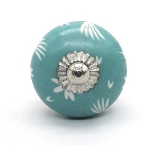 May include: A teal blue ceramic knob with a white floral pattern and a silver metal center.