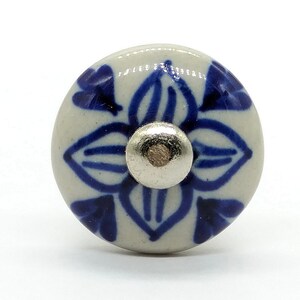 May include: White ceramic knob with a blue and white floral design. The knob has a silver center.