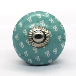 Peut inclure: Un bouton en céramique bleu clair avec un motif de cœurs blancs et un centre en métal argenté.