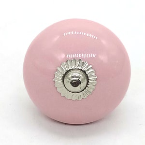 May include: A pink ceramic knob with a silver metal base. The knob is round and has a smooth finish.